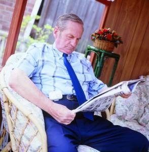 Man sat reading newspaper whilst reading a device that detects falls in the home
