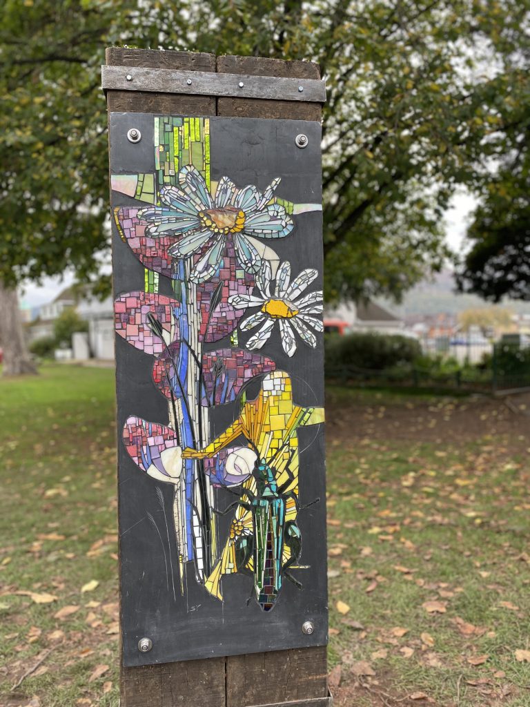 The community artwork, with mosaic flowers, person, and insect, installed in Bailey Park, Abergavenny