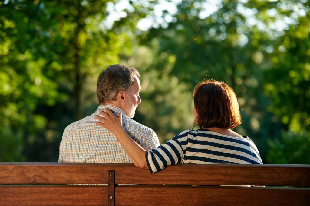 Back view retired senior couple on the bench. Green summer park background.