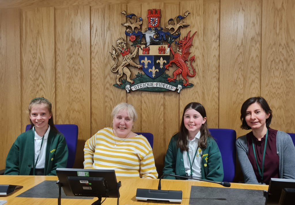 Osbaston pupils accompanied by a parent from the school, with Council Leader Cllr. Mary Ann Brocklesby (centre) in the Council Chamber  Disgyblion o Ysgol Eglwys yng Nghymru Osbaston yn cwrdd â’r Cyng. Mary Ann Brocklesby, Arweinydd y Cyngor