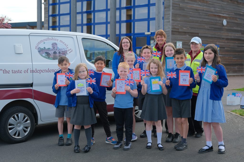 Pupils stand with some of the flags and cards, outside Llanfoist Fawr Primary school, with teacher Victoria Bowen and two of the Monmouthshire Meals team