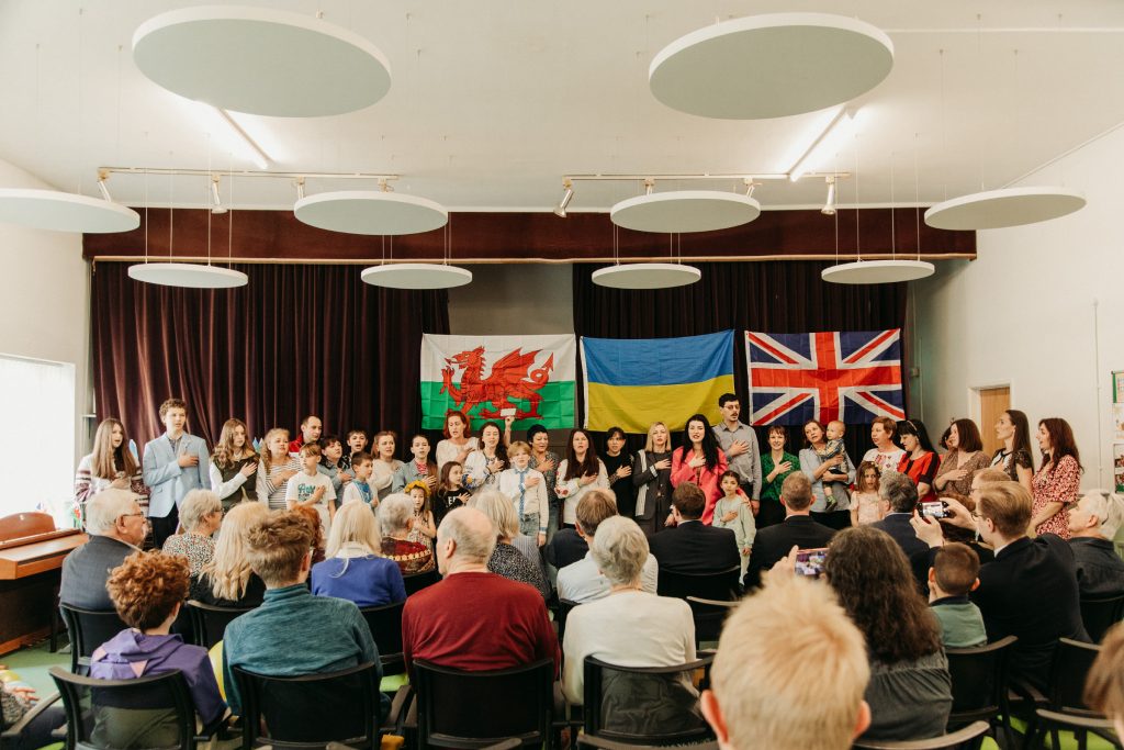 Families gathered in hall - Welsh, Ukraine and British flag are in the background